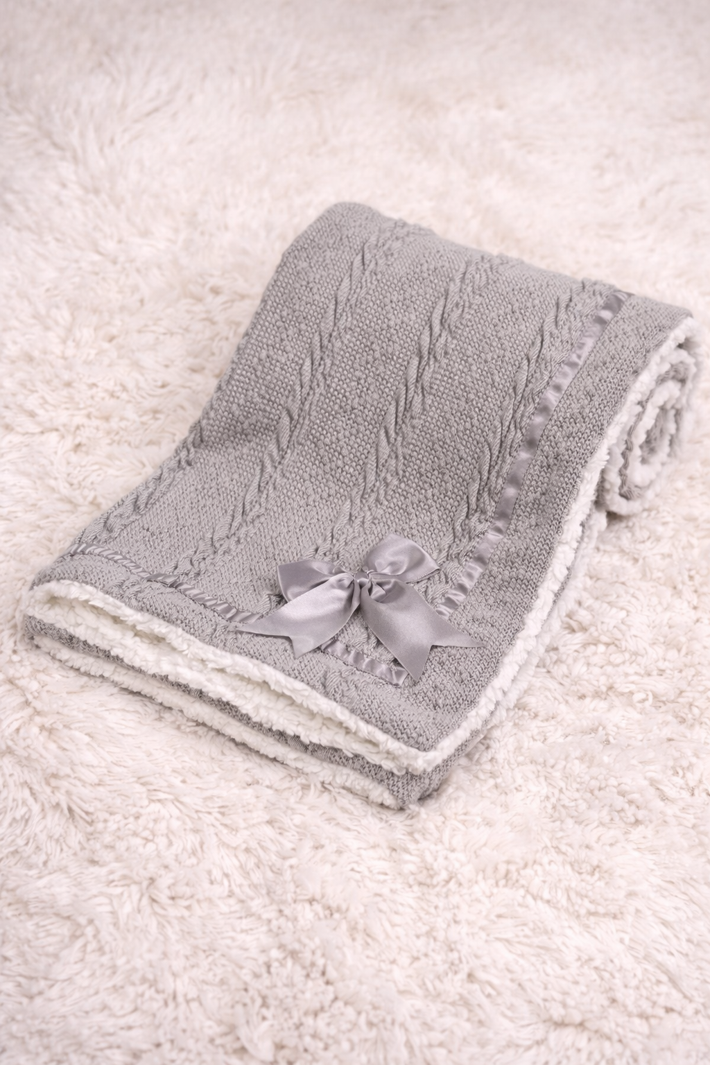 Cosy grey cable knit baby blanket with sherpa lining draped over a sleeping newborn in a pram, ideal for winter walks and newborn comfort.