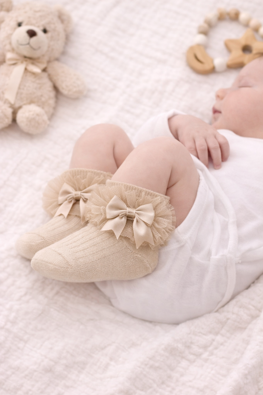 Close-up mock-up of a sleeping newborn baby wearing beige frilly ankle socks with satin bow detail. The socks sit neatly at the ankle with no visible fabric above the frill, styled on a soft neutral blanket for a gentle, minimalist baby aesthetic.