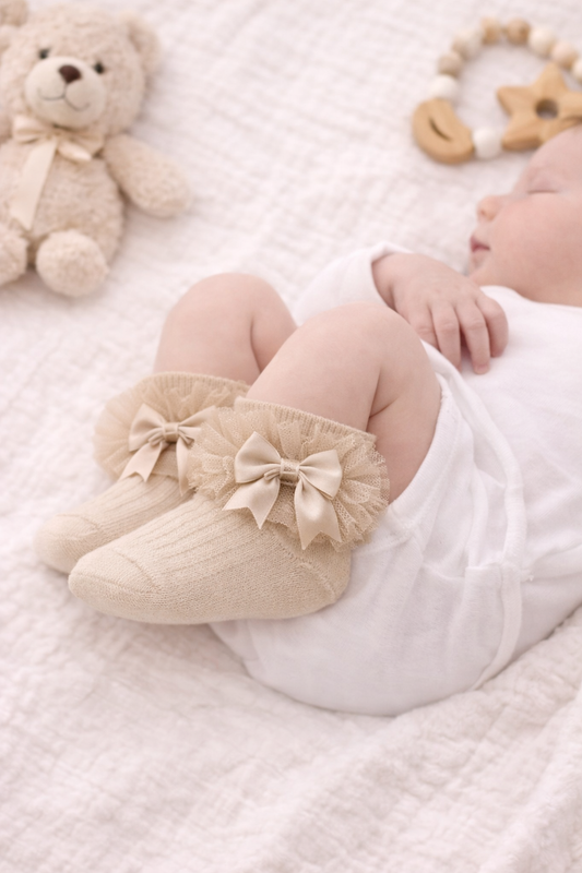 Close-up mock-up of a sleeping newborn baby wearing beige frilly ankle socks with satin bow detail. The socks sit neatly at the ankle with no visible fabric above the frill, styled on a soft neutral blanket for a gentle, minimalist baby aesthetic.