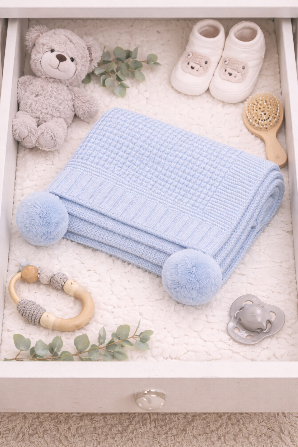 Baby items including a blue blanket, teddy bear, shoes, teether, and pacifier in a drawer.
