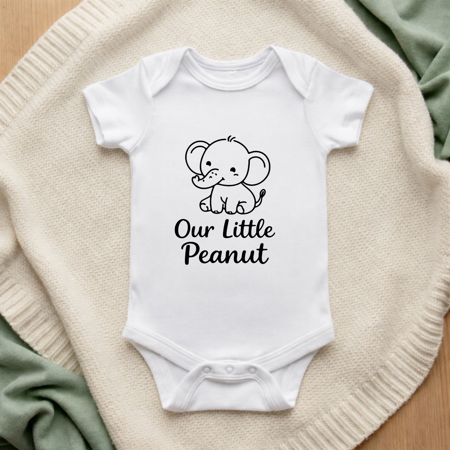 White baby onesie with an elephant graphic and text on a textured surface