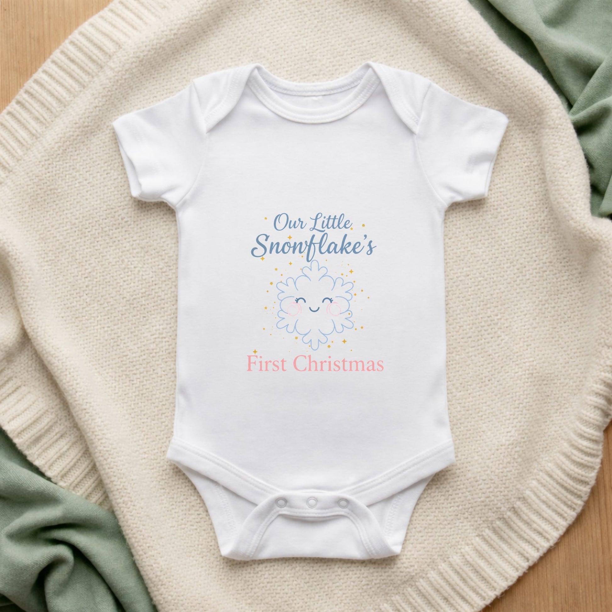 White baby onesie with 'Our Little Snowflake's First Christmas' text on a textured surface.