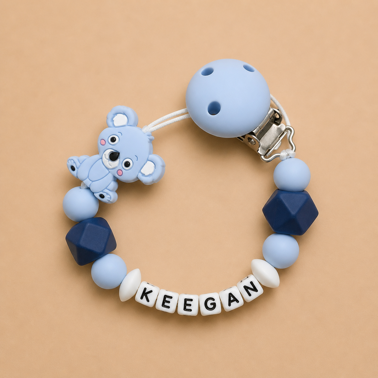 Baby dummy clip with blue and navy beads and a teddy bear charm on a beige background