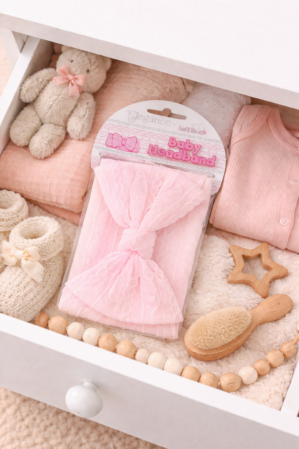 Baby items including a pink bow headband, teddy bear, and wooden toys in a white drawer.