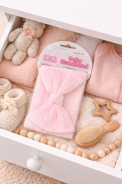 Baby items including a pink bow headband, teddy bear, and wooden toys in a white drawer.