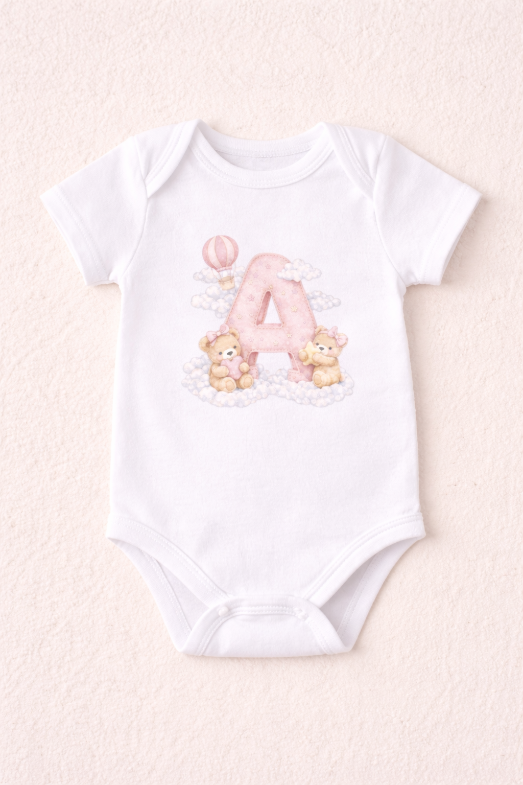 White baby onesie with letter 'A' and teddy bear design on a light pink background