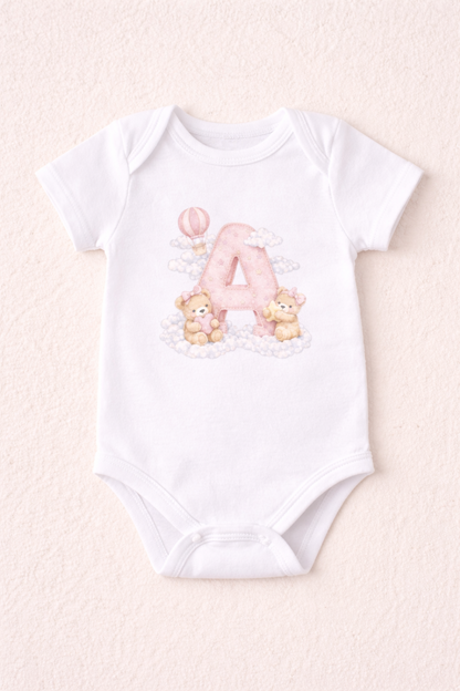White baby onesie with letter 'A' and teddy bear design on a light pink background
