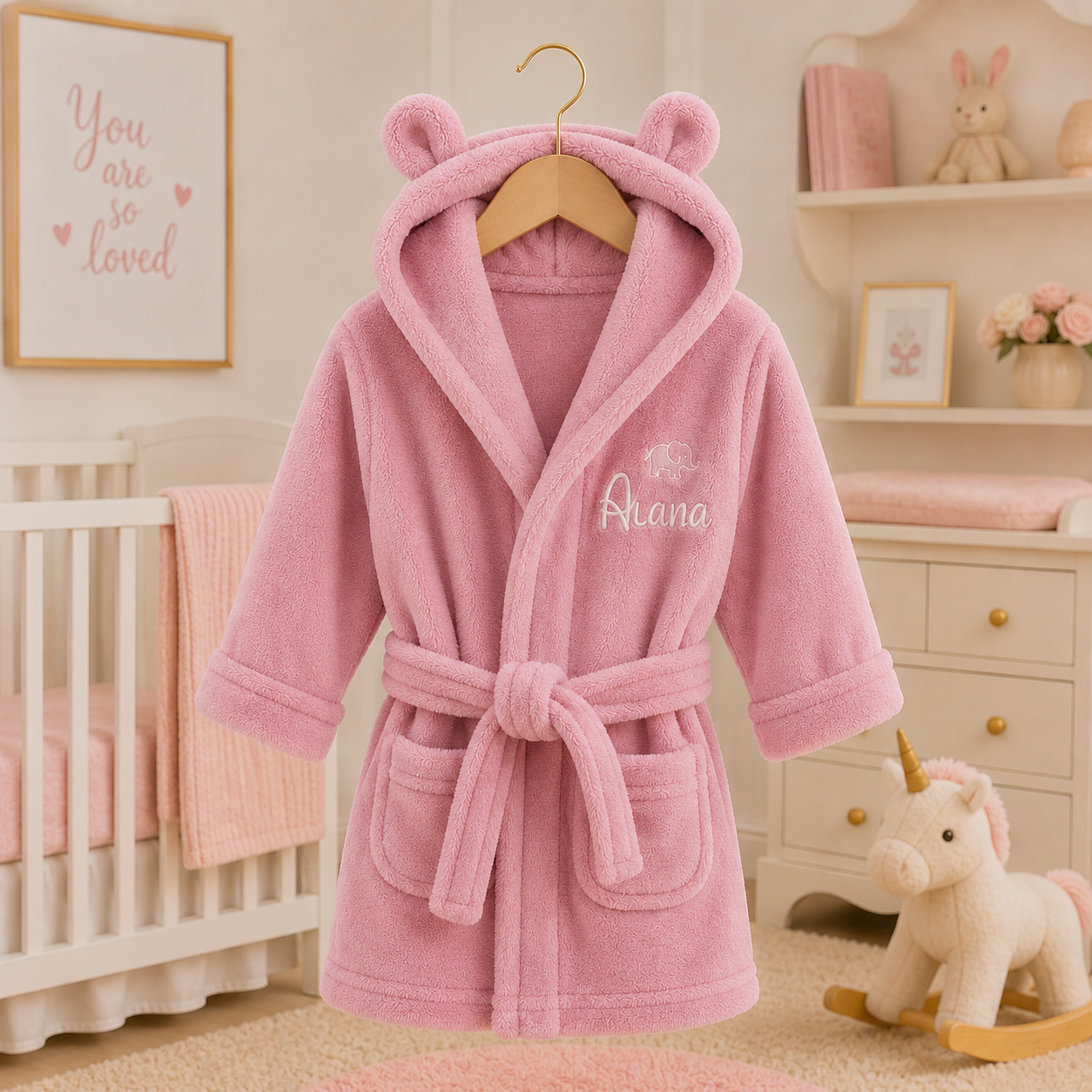 Pink children's robe with bear ears on a hanger in a nursery setting