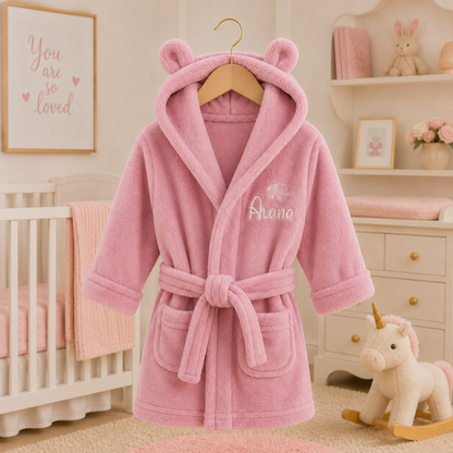 Pink children's robe with bear ears on a hanger in a nursery setting