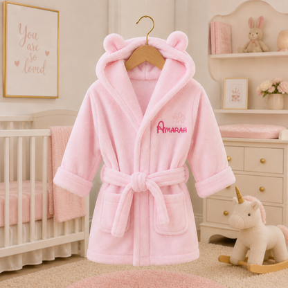 Pink children's robe with bear ears on a hanger in a nursery setting