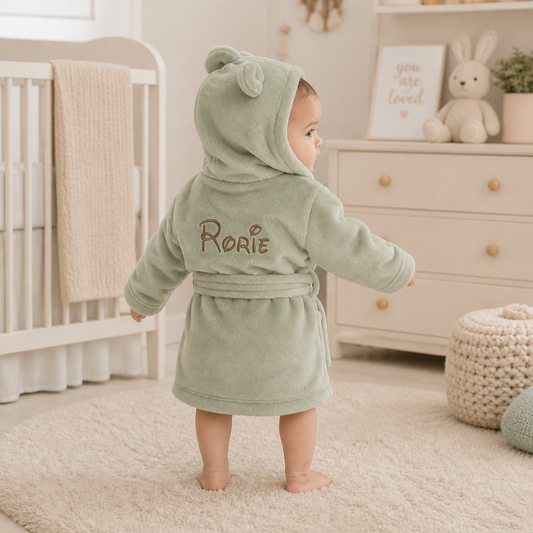 Baby in a green hooded robe with 'Rorie' embroidered in a nursery setting.