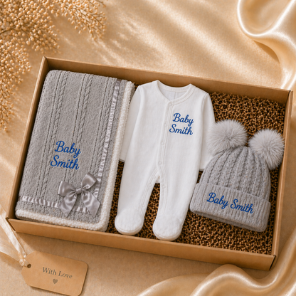 Baby gift set with blanket, romper, and hat in a box on a soft fabric background