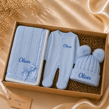 Baby gift set with blue baby blanket, romper, and hat in a box on a beige background