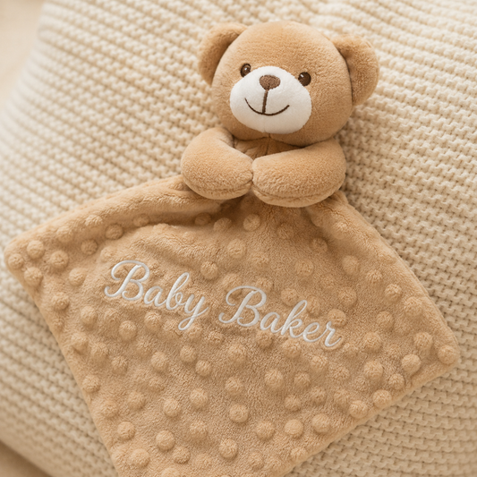 Beige teddy bear security blanket with 'Baby Baker' embroidery on a textured beige background