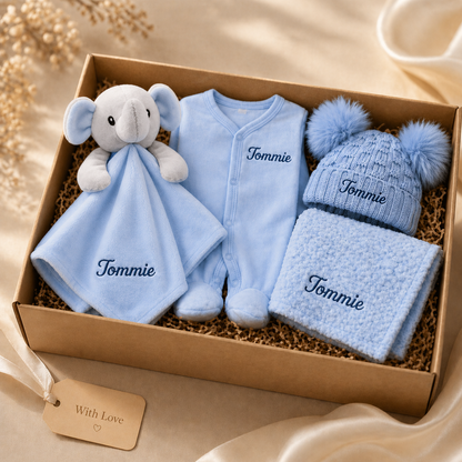 Baby gift set with blue outfit, hat, and blanket in a box on a beige background