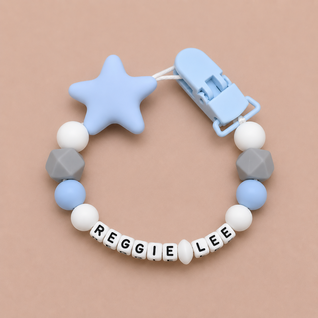 dummy clip with star-shaped blue silicone clip and beads spelling 'REGGIE LEE' on a beige background