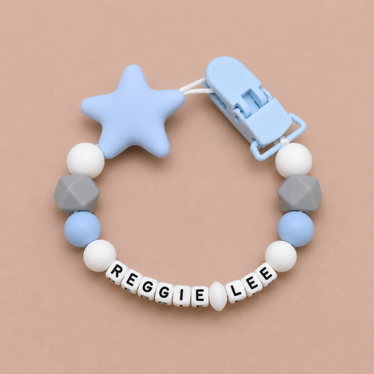 dummy clip with star-shaped blue silicone clip and beads spelling 'REGGIE LEE' on a beige background