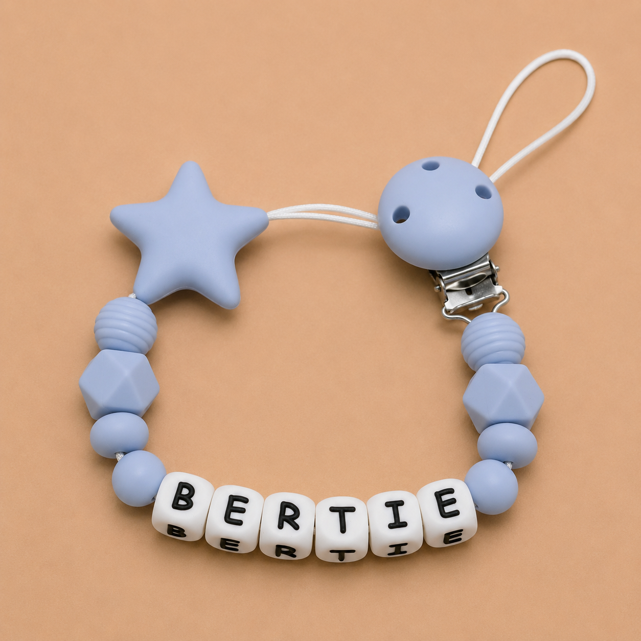 Blue silicone dummy clip with star-shaped bead and 'BERTIE' letter beads on a beige background