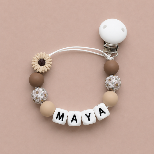Pacifier clip with decorative beads and 'MAYA' letter tiles on a beige background