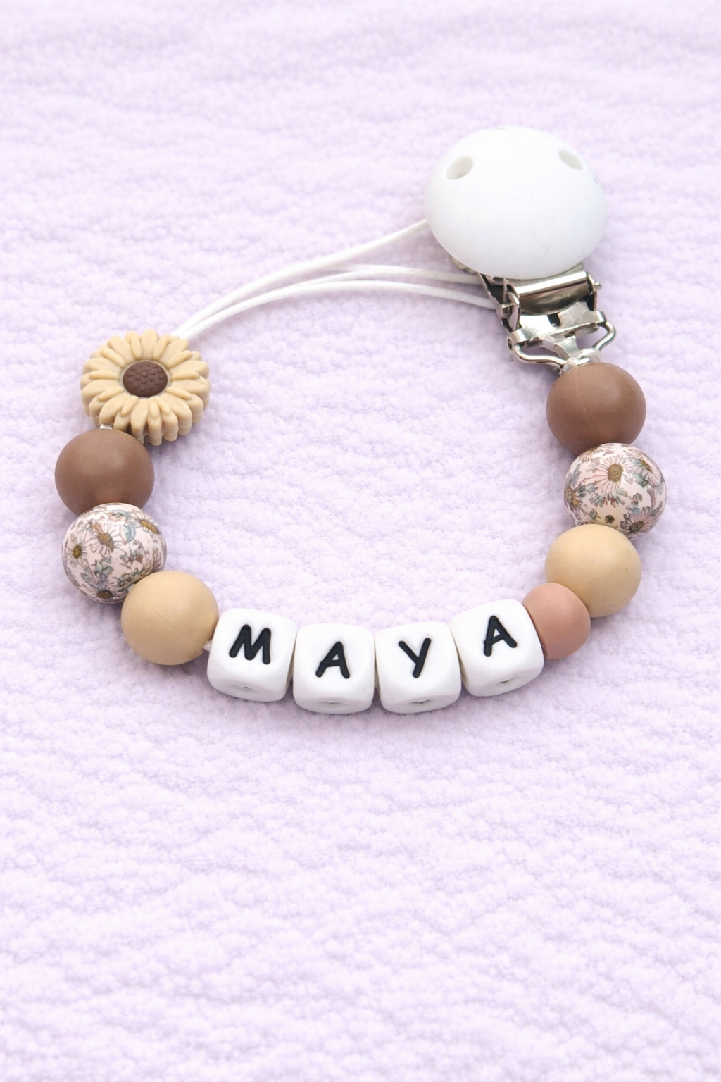 Beaded pacifier clip with 'MAYA' on a light purple background