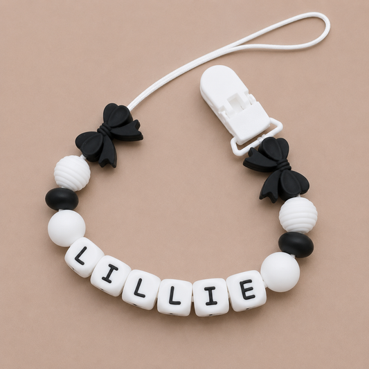 Baby dummy clip with black and white beads and a clip on a beige background