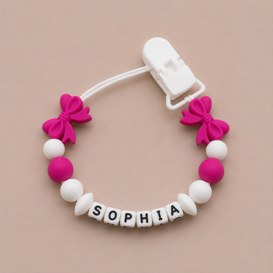 Pacifier clip with pink bows and white beads spelling 'SOPHIA' on a beige background