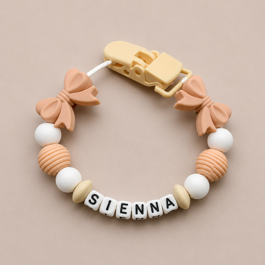 dummy clip with bow-shaped beads and 'SIENNA' letter beads on a beige background