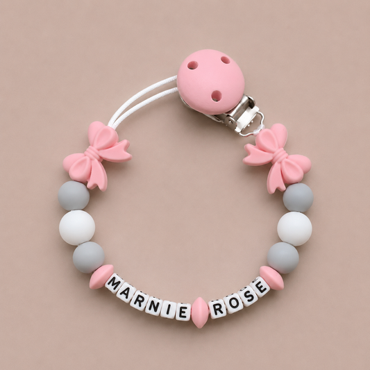 Baby dummy clip with pink and gray beads and 'MARNIE ROSE' letters on a beige background