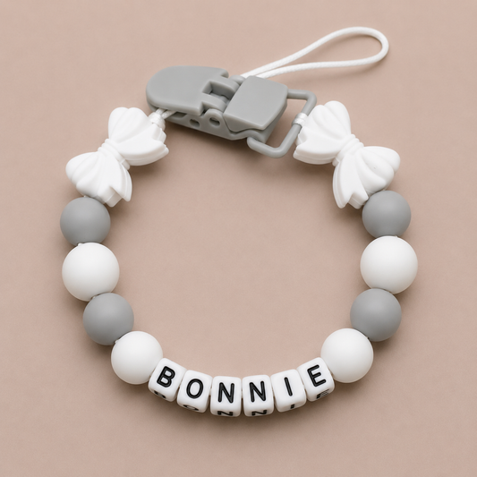 dummy clip with white and gray beads and 'BONNIE' letter beads on a beige background