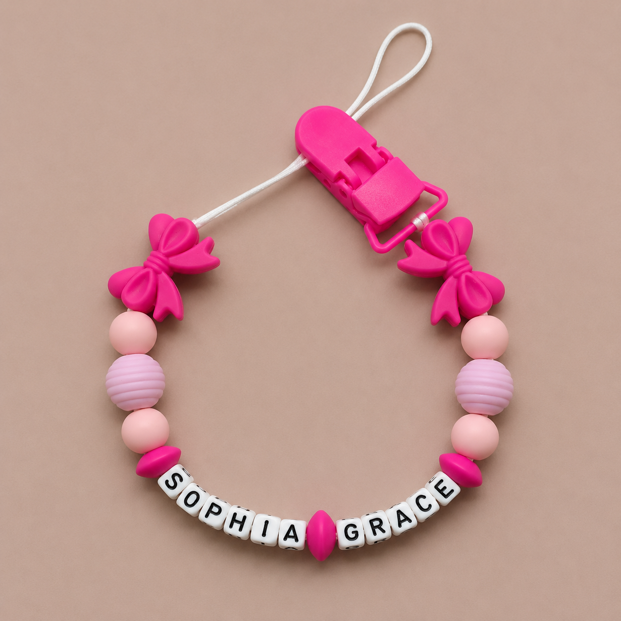 Pink and white dummy clip with 'SOPHIA GRACE' on a beige background