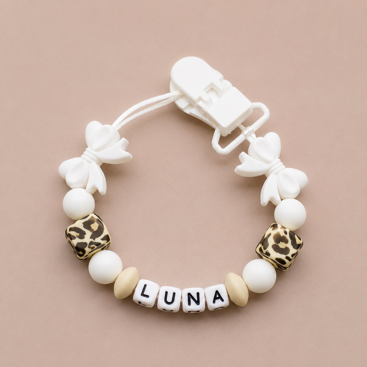 Baby dummy clip with 'LUNA' beads on a beige background