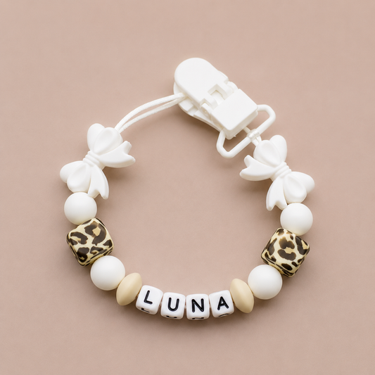 Baby dummy clip with 'LUNA' beads on a beige background