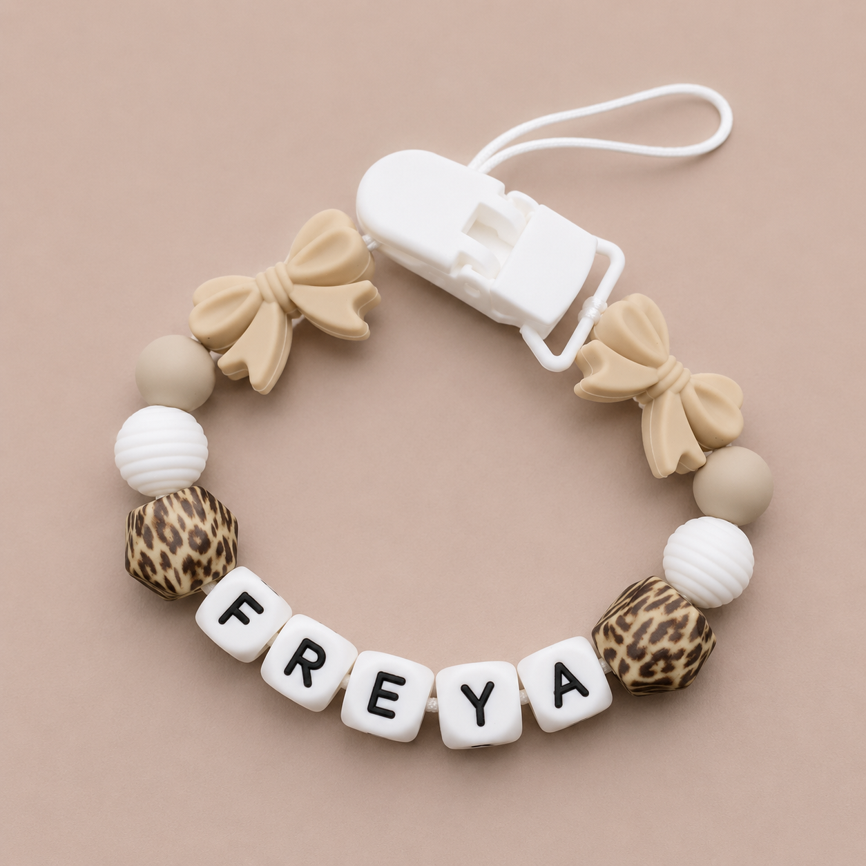 Baby dummy clip with name 'FREYA' on a beige background