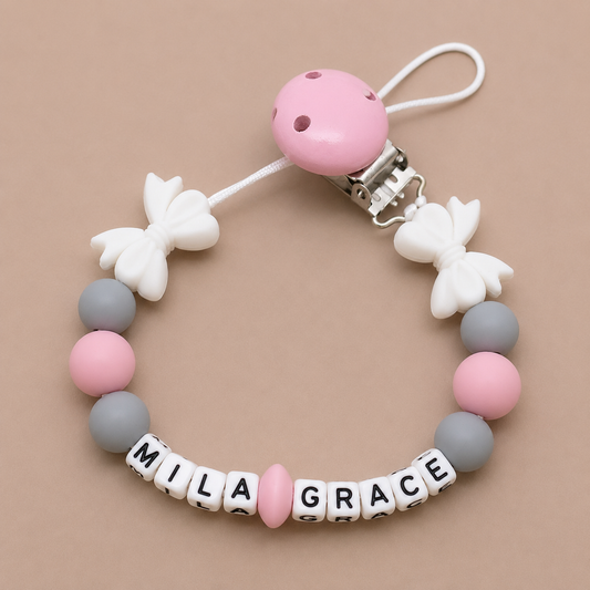 Baby dummy clip with pink and gray beads and 'Mila Grace' letters on a beige background