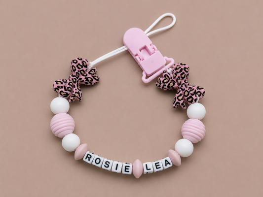 Baby dummy clip with leopard print bows and pink clip on a beige background
