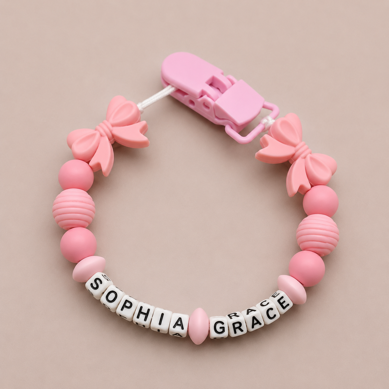 Pink baby dummy clip with 'SOPHIA GRACE' on a beige background