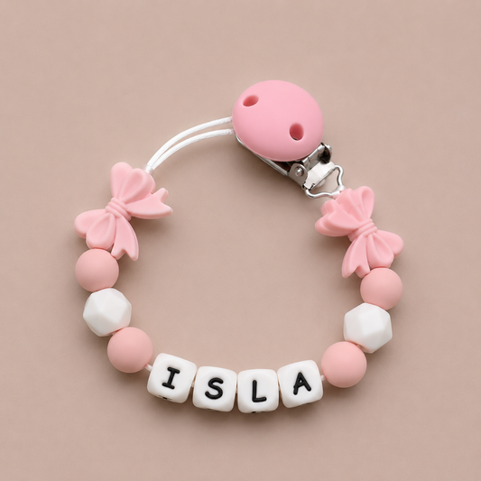 Pink and white pacifier clip with 'ISLA' letter beads on a beige background