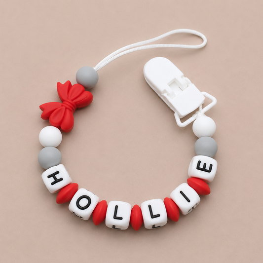Baby dummy clip with 'HOLLY' beads on a beige background