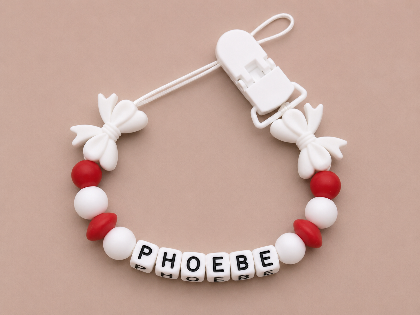 Baby dummy clip with 'PHOEBE' beads on a beige background
