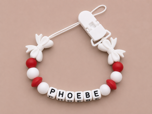 Baby dummy clip with 'PHOEBE' beads on a beige background