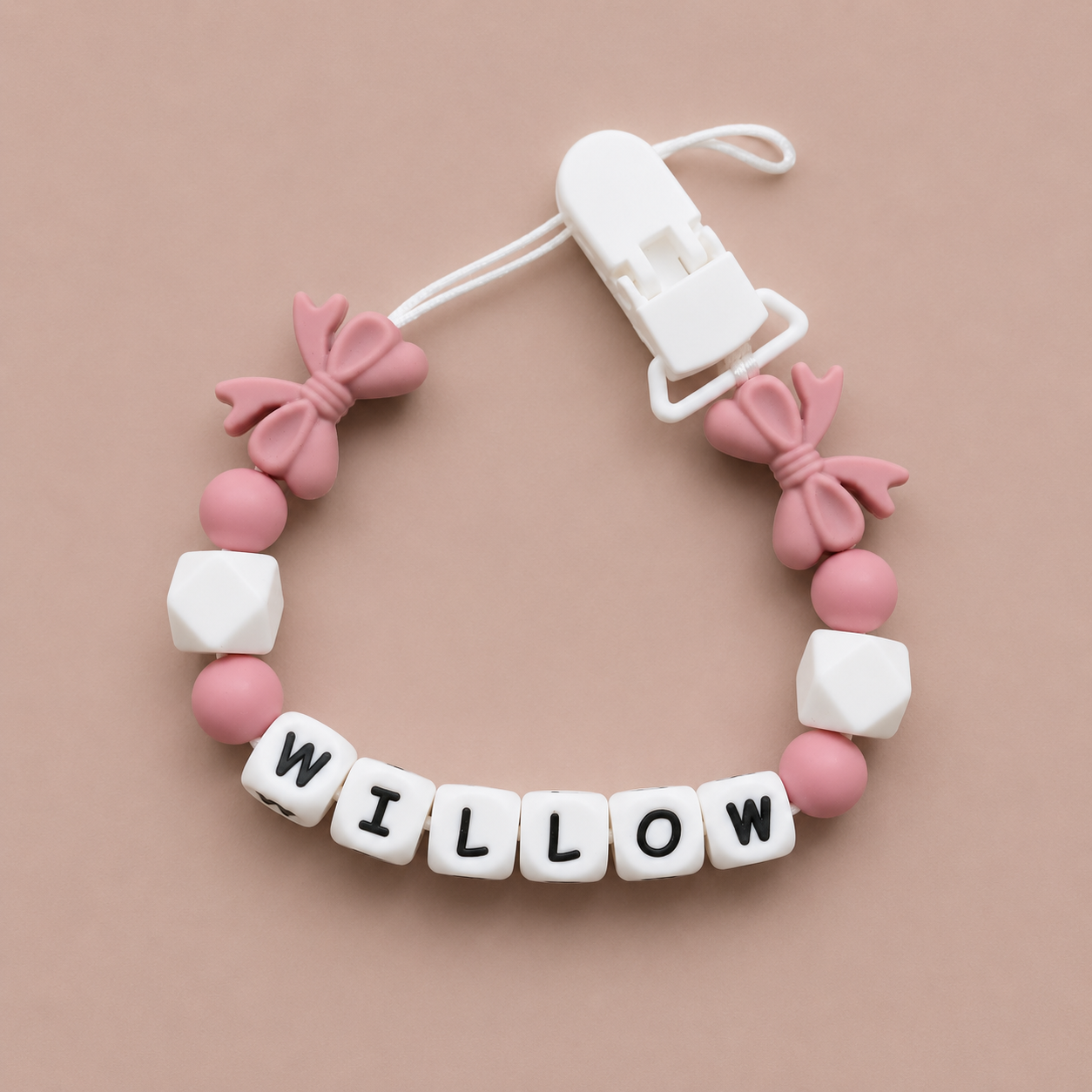 dummy clip with pink and white beads spelling 'WILLOW' on a beige background