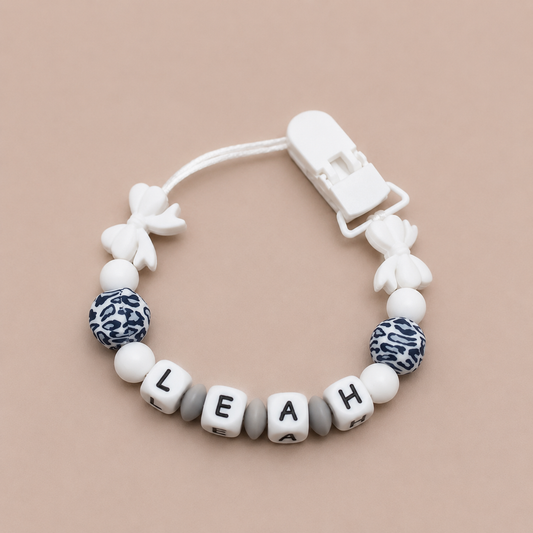 Baby dummy clip with name 'LEAH' on a beige background