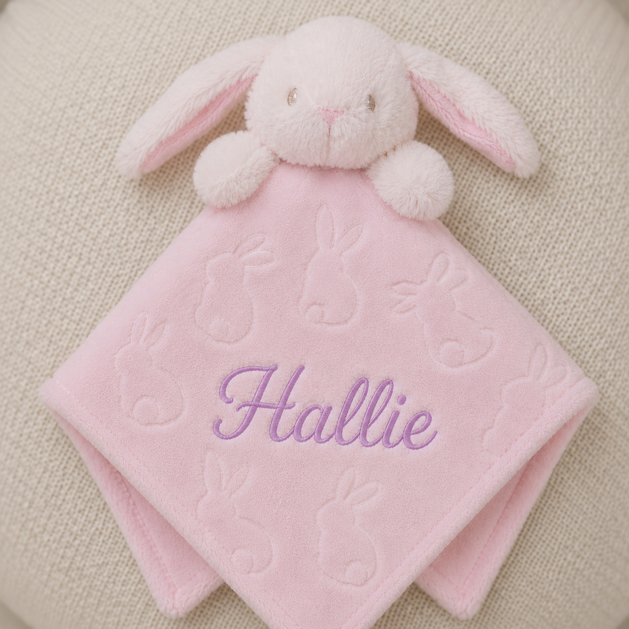 Pink bunny comfort blanket with embroidered name 'Hallie' on a beige background