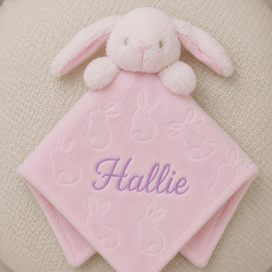 Pink bunny comfort blanket with embroidered name 'Hallie' on a beige background