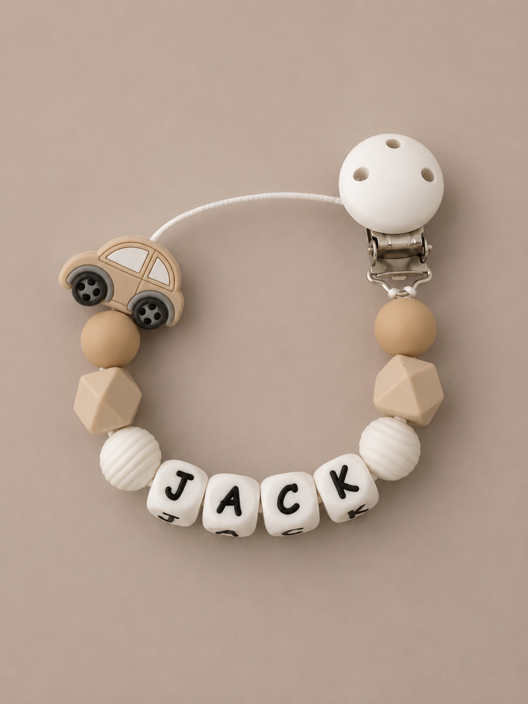 A wooden baby pacifier clip featuring a white plastic clasp, a small wooden car bead, and letter beads spelling 'JACK' on a neutral beige background.