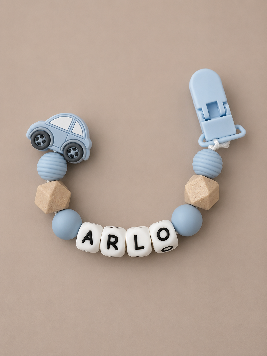A personalized baby pacifier clip featuring a light blue car charm, light blue and beige wooden beads, and white letter beads spelling 'ARLO' on a neutral beige background.