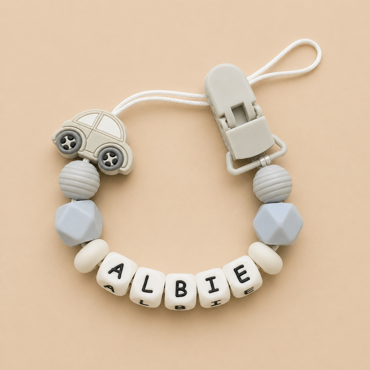 dummy clip with car-shaped bead and letter beads spelling 'ALBIE' on a beige background