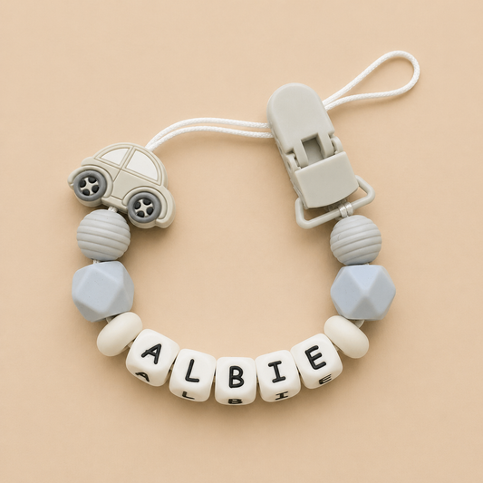 dummy clip with car-shaped bead and letter beads spelling 'ALBIE' on a beige background