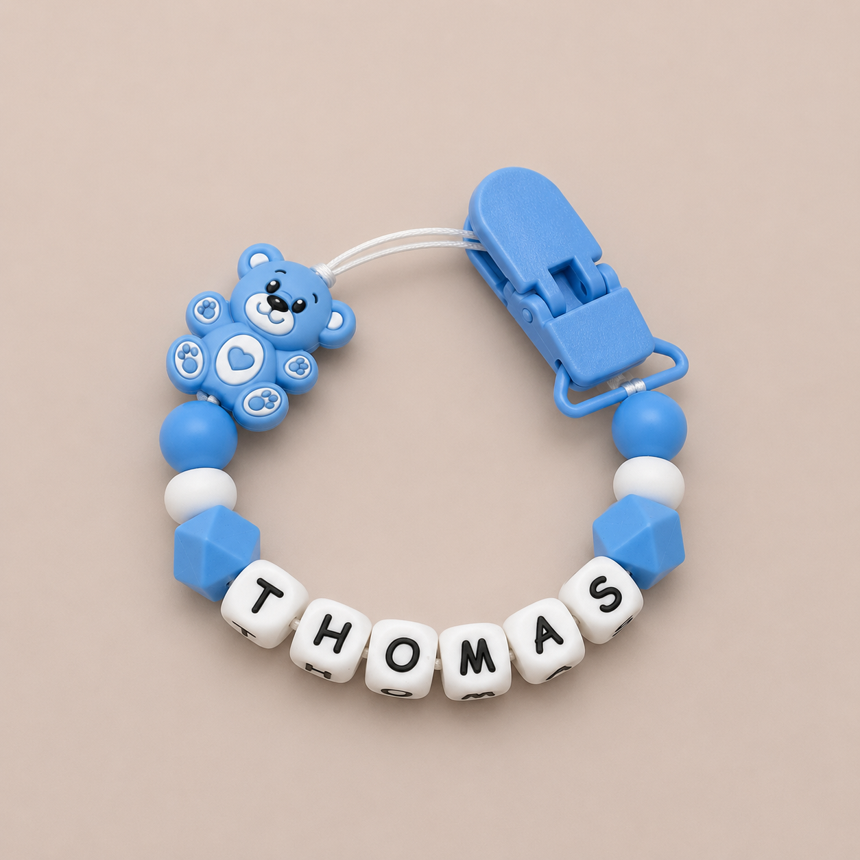 Blue baby dummy clip with 'THOMAS' on a beige background