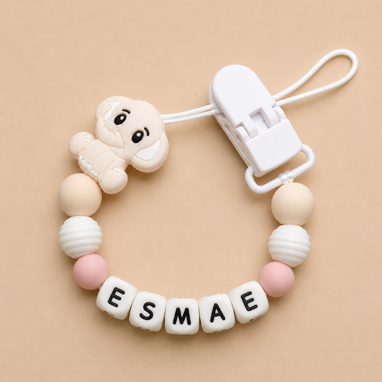 Baby dummy clip with 'ESMAE' on a beige background